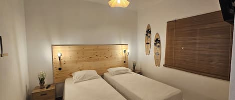 Ein Schlafzimmer mit zwei Betten, einem Holzkopfende, einer Wanddekoration aus einem Surfbrett, einem kleinen Nachttisch mit einer Pflanze und einer Pendelleuchte.