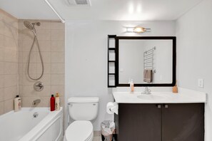 A modern bathroom with a bathtub, toilet, sink, and a large mirror. - StayToronto - Victoria Point Apartments (Toronto)