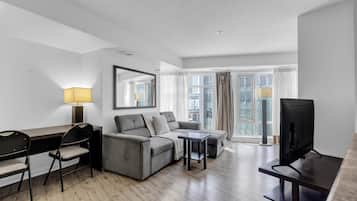 Una habitación de hotel moderna con sofá, escritorio, televisión y un ventanal con cortinas.
