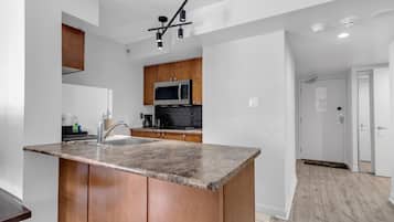 Una cocina moderna con encimera de granito, armarios de madera, microondas integrado y una lámpara colgante.