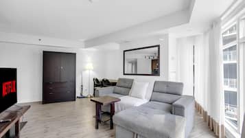 Una sala de estar moderna con un sofá gris, una pequeña mesa de madera, un televisor y un armario oscuro.