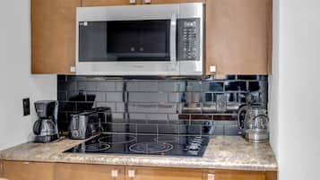 Una cocina con microondas de acero inoxidable, salpicadero de azulejos negros, cocina de inducción negra y armarios de madera.