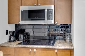 A kitchen with a stainless steel microwave, black tiled backsplash, a black induction cooktop, and wooden cabinets. - StayToronto - Victoria Point Apartments (Toronto)