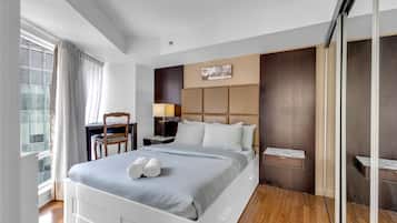 Una habitación de hotel moderna con una cama grande, un escritorio, una silla, una mesita de noche y un ventanal con cortinas.