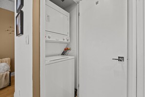 A laundry room with a dryer and a washing machine, a door with a handle, and a small shelf with items on it. - Victoria Point Apartments (Toronto)