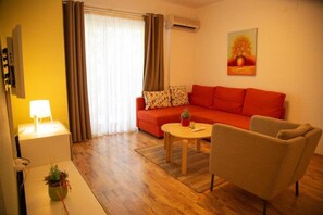 Una sala de estar con un sofá rojo, un sillón color beige, una mesita redonda y una lámpara.