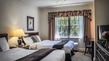 A hotel room with two beds, a desk, a chair, a television, and a window with curtains.