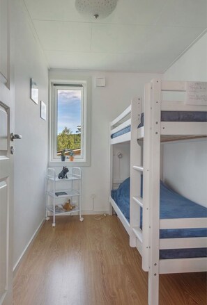 Ein Zimmer mit Etagenbett, einem Fenster mit Blick auf Grünflächen, einem kleinen Schreibtisch mit Stuhl und einem Regal mit einer Hundefigur.