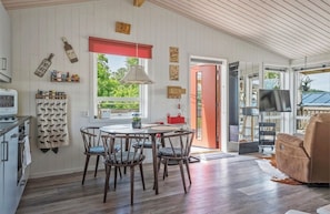 A cozy kitchen with wooden cabinets, a dining table with chairs, and a red-framed window. - Lakeside Retreat on Lake Laxsjön – Lake Views, Kayaks & Private Heated Terrace (Dals Långed)