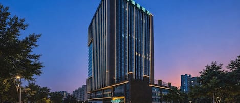 Un edificio hotelero alto de diseño moderno, con una entrada destacada y varios pisos.