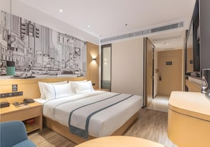Ein Hotelzimmer mit einem großen Bett, einem Schreibtisch mit Telefon und einem wandmontierten Fernseher.