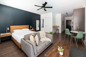 A modern hotel room with a bed, a grey sofa, a dining area with a table and chairs, and a ceiling fan. - Locale Nashville - Music Row (Nashville)