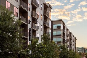 Un edificio residencial de varios pisos con balcones, un cartel que indica 'Music Row' y árboles en primer plano.