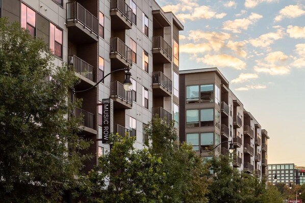 A multi-story residential building with balconies, a sign indicating 'Music Row,' and trees in the foreground. - Locale Nashville - Music Row (Nashville)