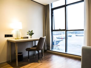 A hotel room with a desk, chair, lamp, potted plant, and a large window with a view of boats and water. - GYA Ningbo Xiangshan Shipu Hotel (Ningbo)
