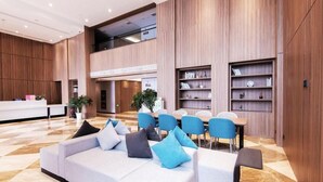 Um saguão moderno de hotel com balcão de recepção, área de estar e estantes embutidas.