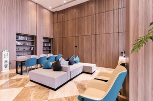Un moderno vestíbulo de hotel con un sofá seccional, sillas azules, una mesita y estanterías empotradas.