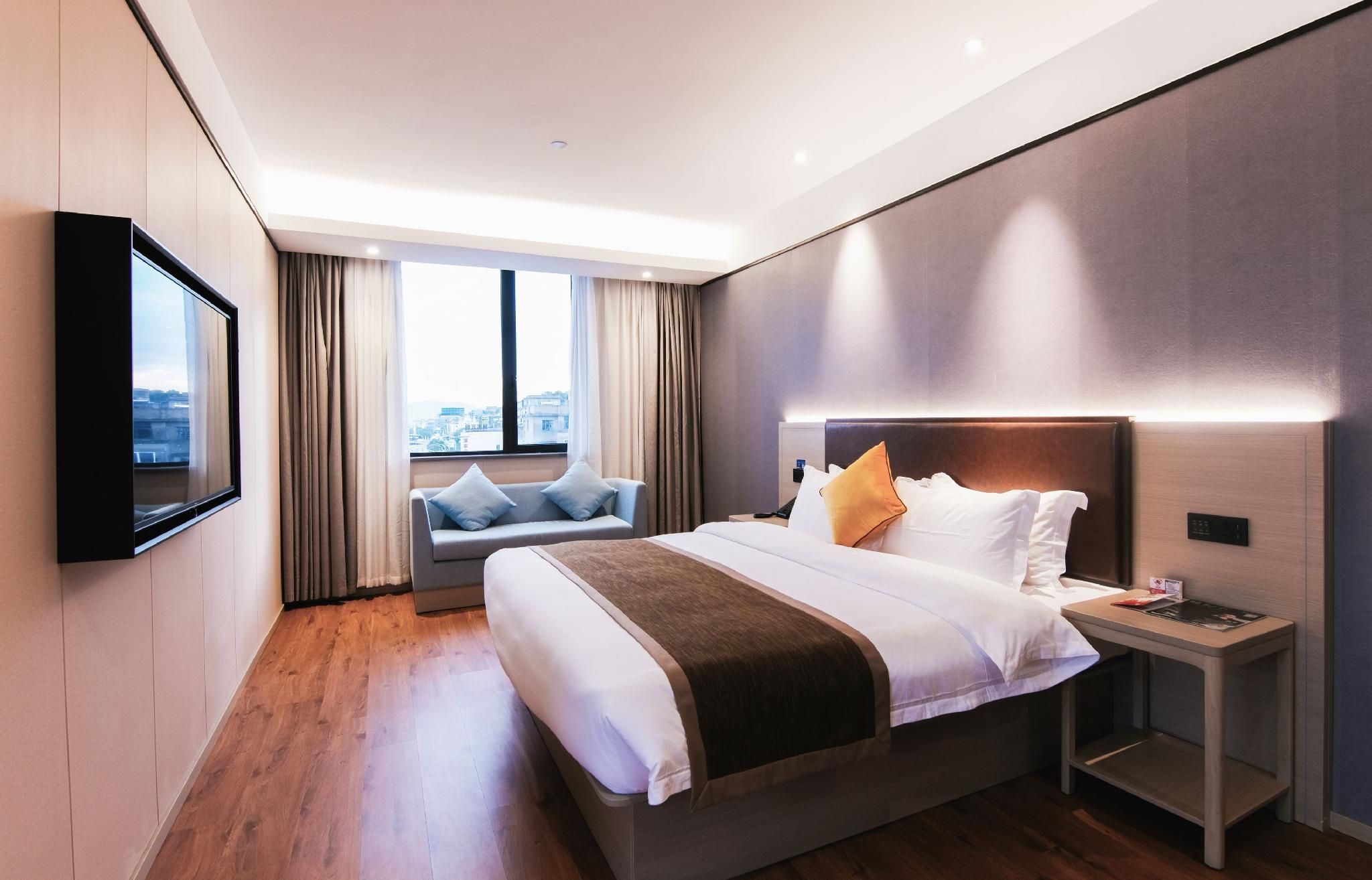 Quarto de hotel moderno com uma cama grande, mesa de cabeceira, TV na parede e janela com vista para a cidade.