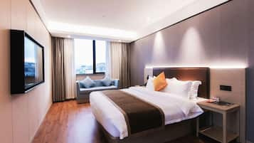 Quarto de hotel moderno com uma cama grande, mesa de cabeceira, TV na parede e janela com vista para a cidade.