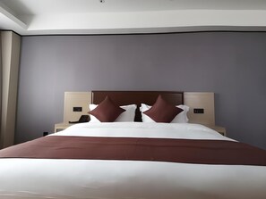 Habitación de hotel moderna con una cama grande, un cabecero, mesitas de noche y una mesita con teléfono.