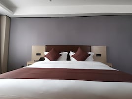Habitación de hotel moderna con una cama grande, un cabecero, mesitas de noche y una mesita con teléfono.