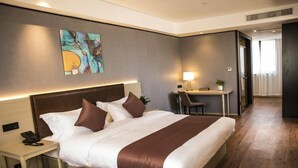 Quarto de hotel com cama grande, mesa de cabeceira, escrivaninha e uma cadeira.