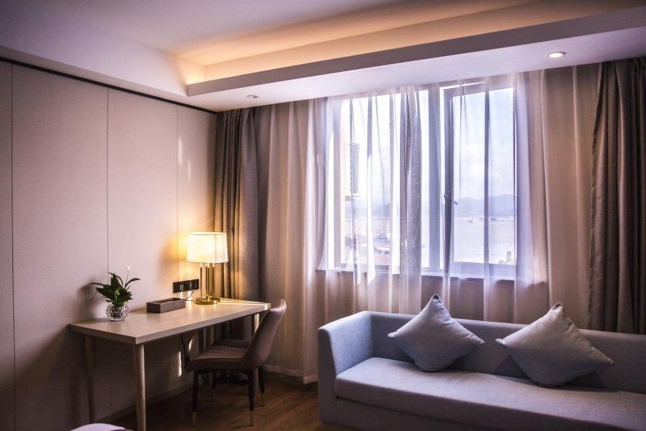 Een hotelkamer met een bureau, een stoel, een bank en een raam met gordijnen.