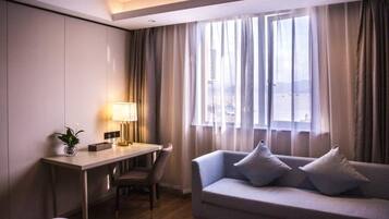 Een hotelkamer met een bureau, een stoel, een bank en een raam met gordijnen.