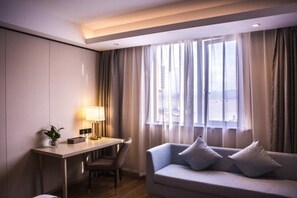 Una habitación de hotel con escritorio, una silla, un sofá y una ventana con cortinas.