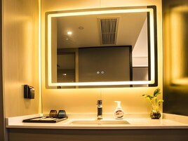 Un baño moderno con un espejo grande, un lavabo, un grifo, un dispensador de jabón y una planta pequeña.