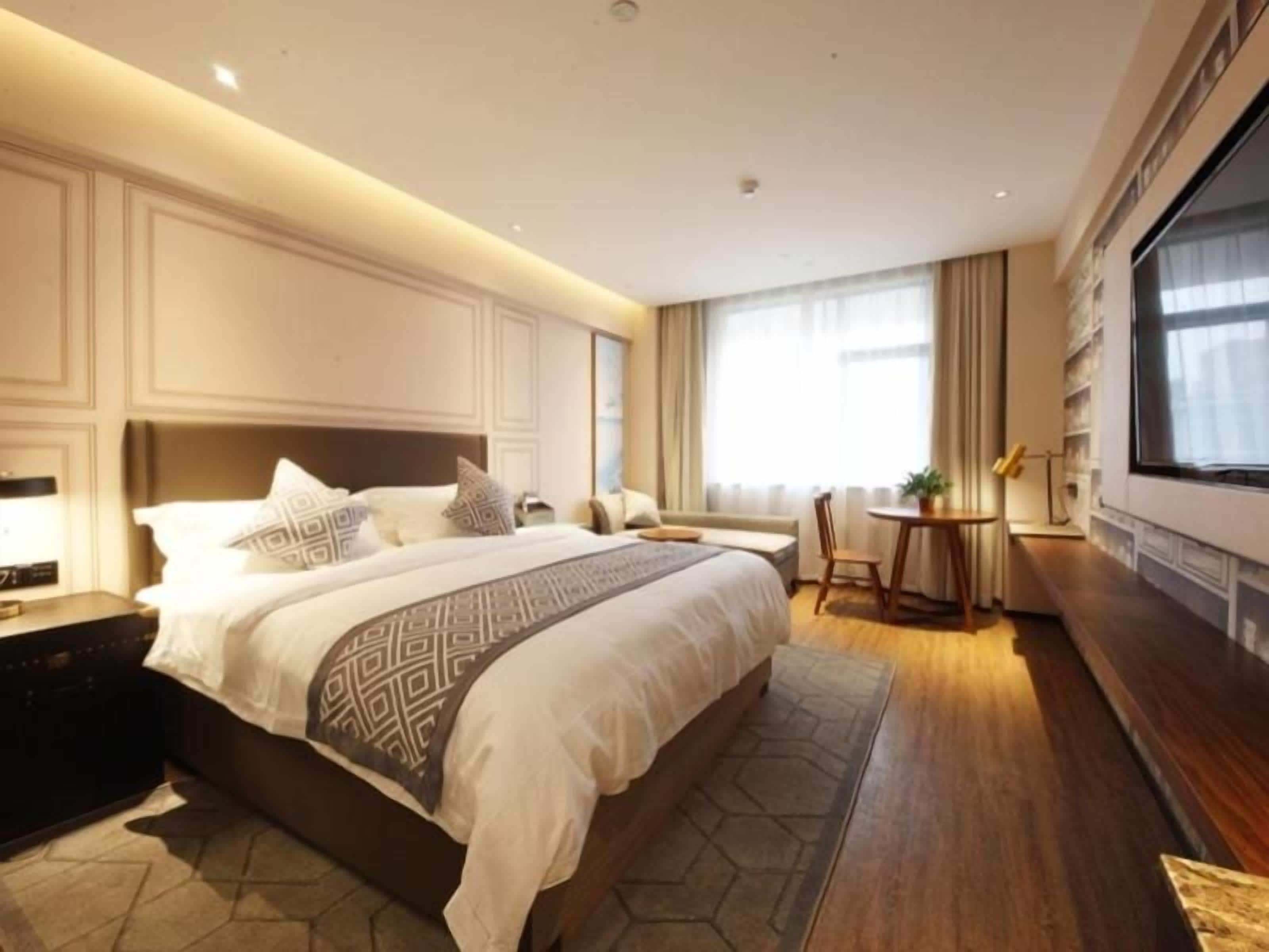 Et moderne hotelværelse med en stor seng, sengeborde, et siddeområde og et stort vindue.