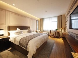 Un dormitorio de hotel moderno con una cama grande, mesitas de noche, una zona de estar y un ventanal amplio.