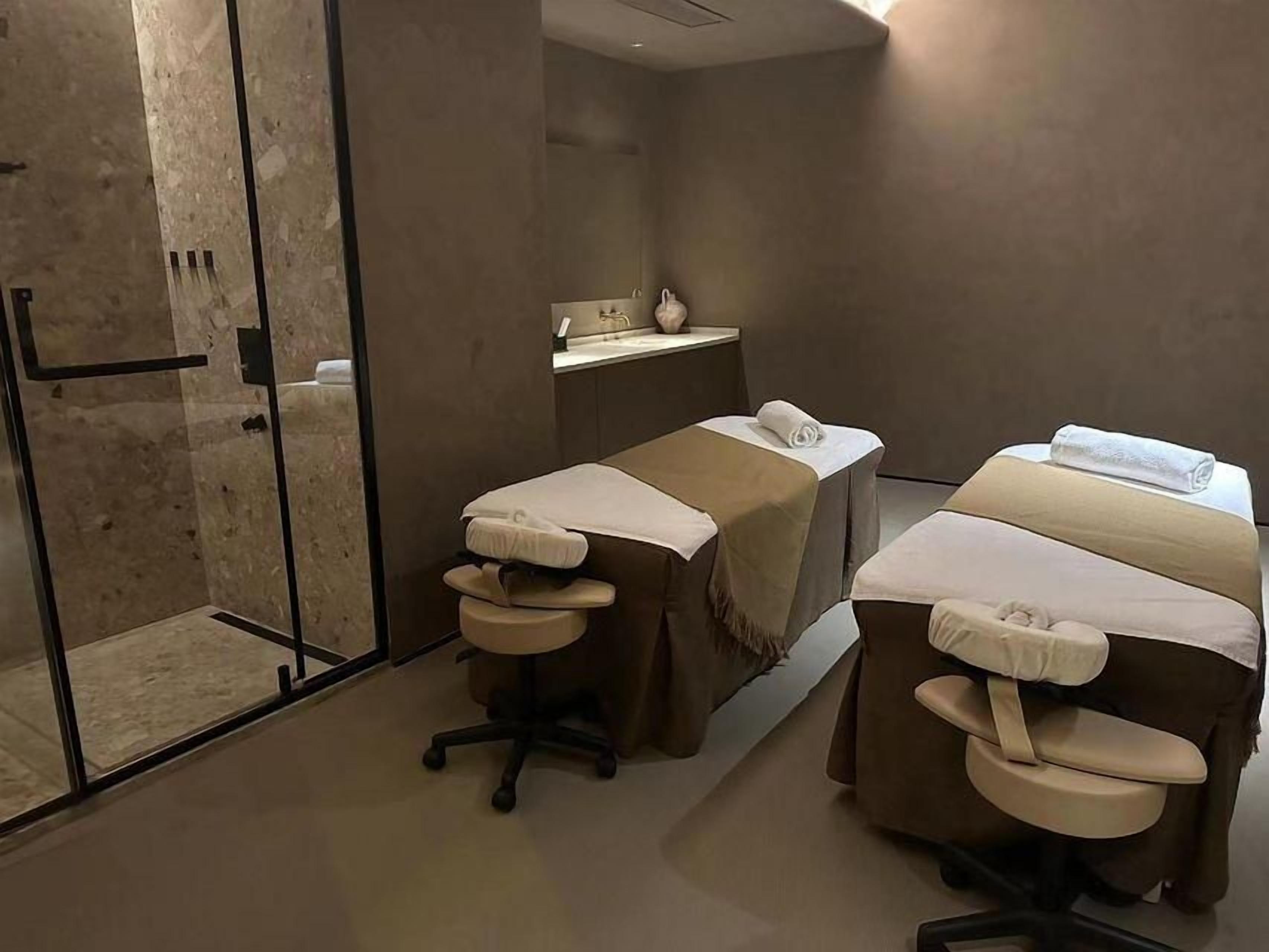 A spa room with two massage tables, a glass shower enclosure, and a small sink area.