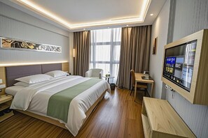 Una habitació d'hotel amb un llit, escriptori, cadira, televisió i finestra amb cortines.