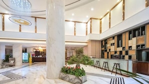 A spacious lobby with a marble floor, a central column, a reception desk, and a seating area with stools. - Metropolo Jinjiang Hotels (Xuzhou)
