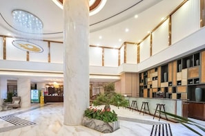 A spacious lobby with a marble floor, a central column, a reception desk, and a seating area with stools. - Metropolo Jinjiang Hotels (Xuzhou)