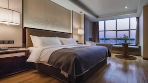 Une chambre d’hôtel avec un grand lit, une table de chevet, une commode, une lampe et une vue sur la ville.
