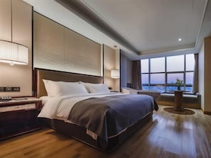 Habitación de hotel con una cama grande, una mesita de noche, una lámpara y vistas a la ciudad.
