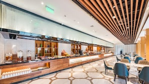 Un hall d’hôtel moderne avec un long comptoir d’accueil, un espace salon et un plafond décoratif.