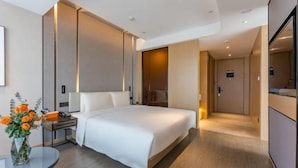 A modern hotel room with a large bed, bedside tables, a mirror, and a small table with a vase of flowers. - Atour Hotel Yiwu International Trade City Passenger Transport Center (Jinhua)