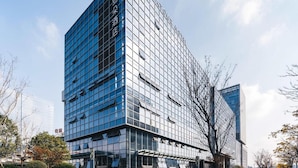 A modern hotel building with a glass facade, a prominent entrance, and a parking area in front. - Atour Hotel Yiwu International Trade City Passenger Transport Center (Jinhua)
