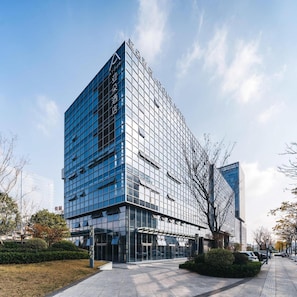En moderne hotels bygning med en glasfacade, en markant indgang og en parkeringsplads foran.