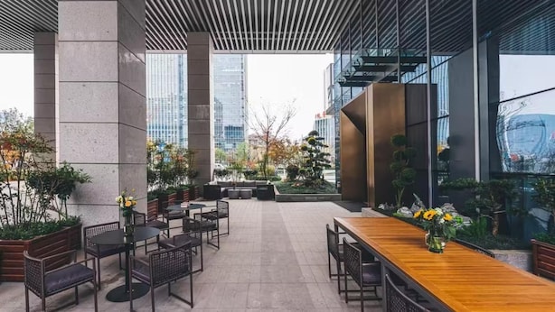 An outdoor seating area with tables and chairs, surrounded by potted plants and a modern building facade. - Atour Hotel Yiwu International Trade City Passenger Transport Center (Jinhua)