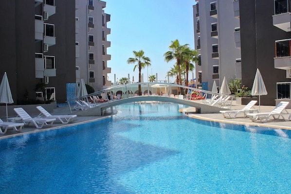 Una piscina amb gandules i ombrel·les, envoltada d'edificis alts.