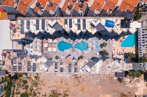 Vista aérea de un hotel con múltiples piscinas, tumbonas y una terraza en la azotea.