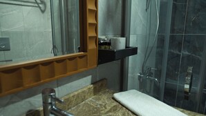 Un bany amb taulell de marbre, un rentapeus blanc, un mirall i una zona de dutxa.