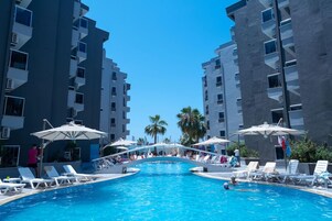 Una piscina con sillones de descanso y sombrillas, rodeada de edificios altos.