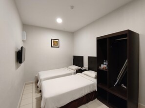 Una habitació d'hotel amb dos llits individuals, un armari, una taula de nit amb una làmpada i un televisor fixat a la paret.