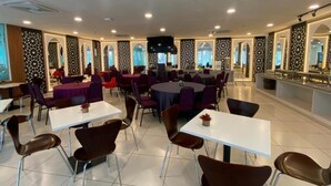 A spacious dining area with multiple tables and chairs, a central stage, and a kitchen area. - Hotel Desaru Penawar (Bandar Penawar)