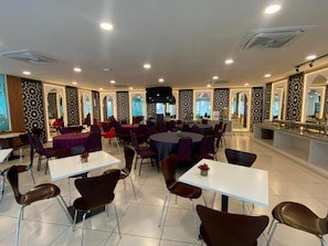 A spacious dining area with multiple tables and chairs, a central stage, and a kitchen area. - Hotel Desaru Penawar (Bandar Penawar)